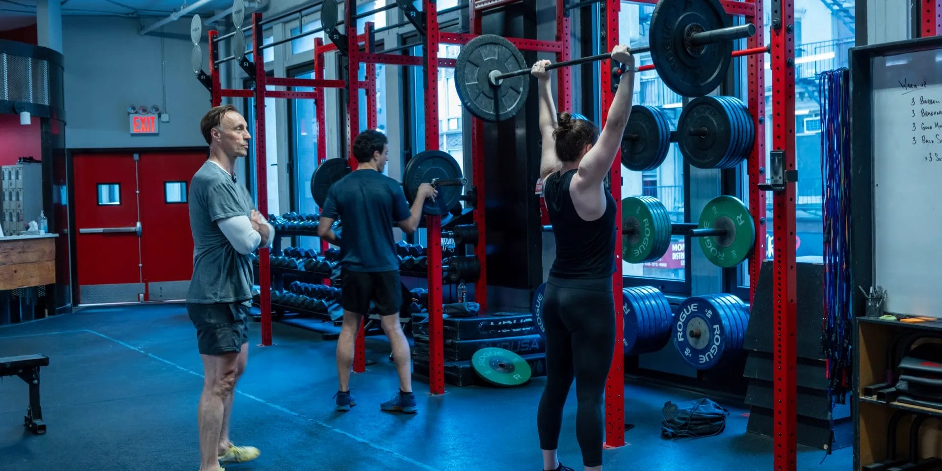 Woman lifting barbell with coach supervision