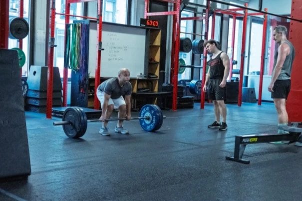 Man lifting barbell with coaches supervision